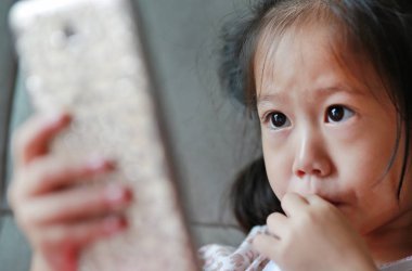 Akıllı telefon çalmaya ve gri kanepe evde içme sütü saman ile sevimli küçük çocuk kız.