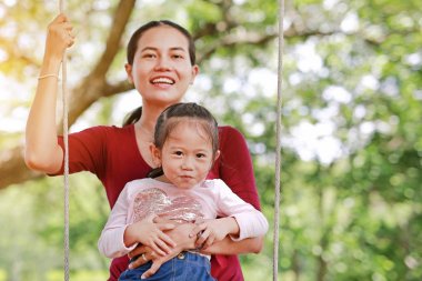 Mutlu Asya anne ve kızı, güneş ışınları ile bahçede sallanan yalan.