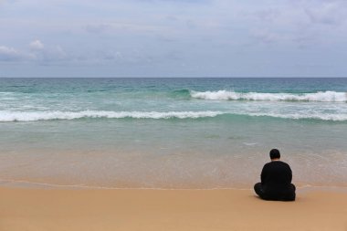Sahilde oturan siyah elbiseli görünümü yalnız kadın geri.