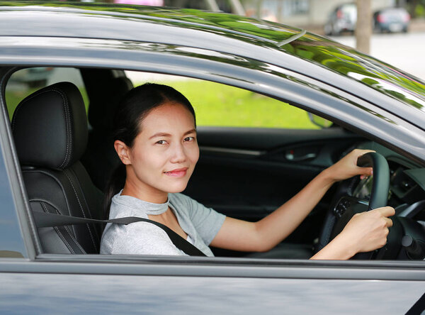 Beautiful asian woman driving a car with looking camera and smiling.