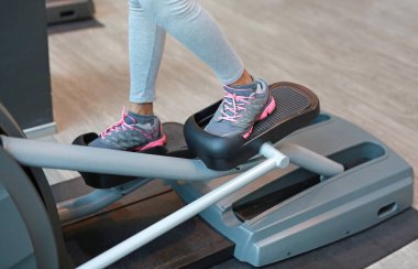 Spor salonunda bir egzersiz makinede çalışan, kas bacaklı kadın.