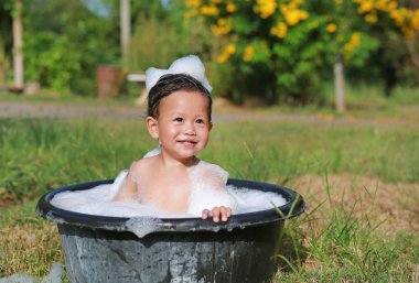 Mutlu Asyalı bebek köpükle banyo yapar ve doğada siyah plastik havuzda yıkanır..