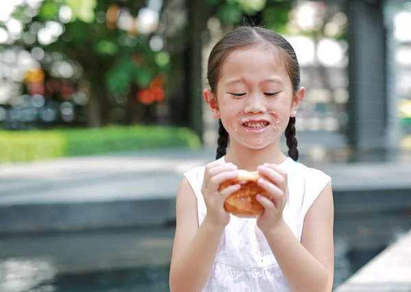 快乐的亚洲小女孩吃面包与填充草莓填充甜点和沾染在她的嘴在花园户外 — 图库照片