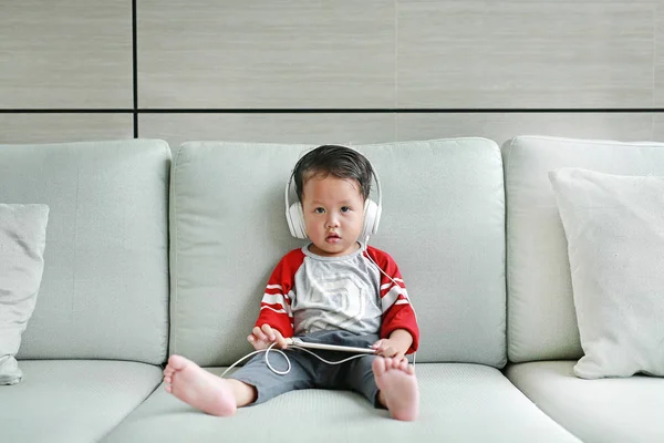Adorable Little Baby Boy Headphones Using Smartphone Lying Sofa Home — Stockfoto