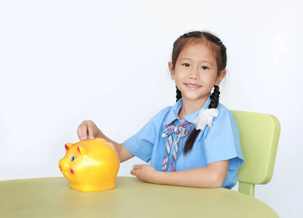 Uśmiechnięta Azjatka Szkolnym Mundurze Siedząca Stole Wkładająca Monety Skarbonki Odizolowana — Zdjęcie stockowe