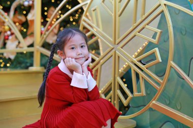 Kırmızı elbiseli küçük kızın portresi kış mevsiminde poz veriyor ve yeni yıl festivali yılbaşı arkaplanına karşı kutlanıyor..