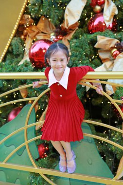 Kırmızı elbiseli neşeli Asyalı küçük kız kış mevsiminde eğleniyor ve yeni yıl festivalinde Noel arkaplanına karşı mutlu yıllar..