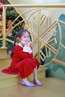 Kırmızı elbiseli mutlu küçük kızın portresi kış mevsiminde poz veriyor ve yeni yıl festivalinde Noel arkaplanına karşı mutlu pozlar veriyor..