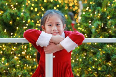 Kırmızı elbiseli neşeli Asyalı küçük kız kış mevsiminde eğleniyor ve yeni yıl festivalinde Noel arkaplanına karşı mutlu yıllar..