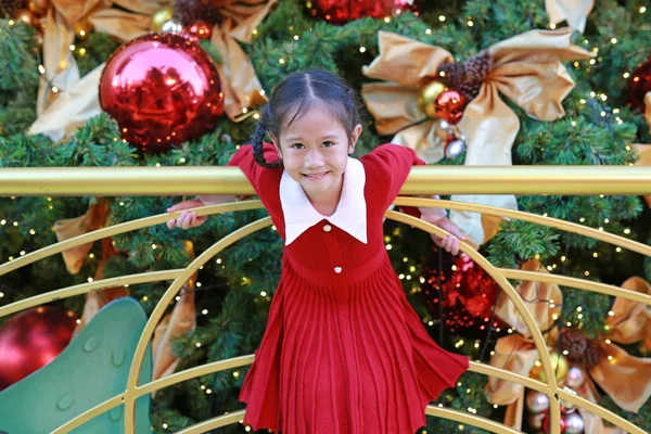 Kırmızı elbiseli neşeli Asyalı küçük kız kış mevsiminde eğleniyor ve yeni yıl festivalinde Noel arkaplanına karşı mutlu yıllar..