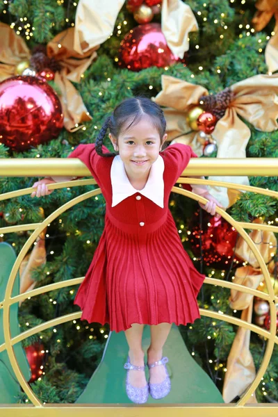 Kırmızı elbiseli mutlu Asyalı küçük kız kış mevsiminde eğleniyor ve yeni yıl festivalinde Noel arkaplanına rağmen mutlu yıllar..