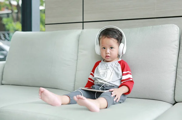 Roztomilý Malý Asijský Chlapeček Sluchátkách Používá Smartphone Ležící Doma Pohovce — Stock fotografie