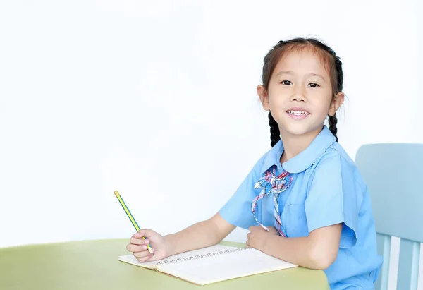 Glad Asiatisk Liten Flicka Skoluniform Skriva Anteckningsbok Vid Skrivbordet Isolerad — Stockfoto