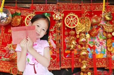 Küçük mutlu Asyalı kız çocuğu geleneksel pembe Cheongsam elbisesi giyerken gülümserken Çin şans çantasından kırmızı zarf paketi alıyor. Mutlu Çin Yeni Yıl Konsepti.