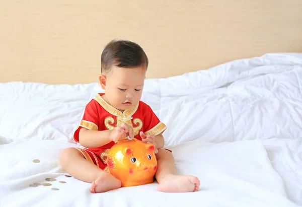 身穿中国传统服装的亚洲小男孩把一些硬币放进了家里的储蓄罐里 小孩子存钱的概念 — 图库照片