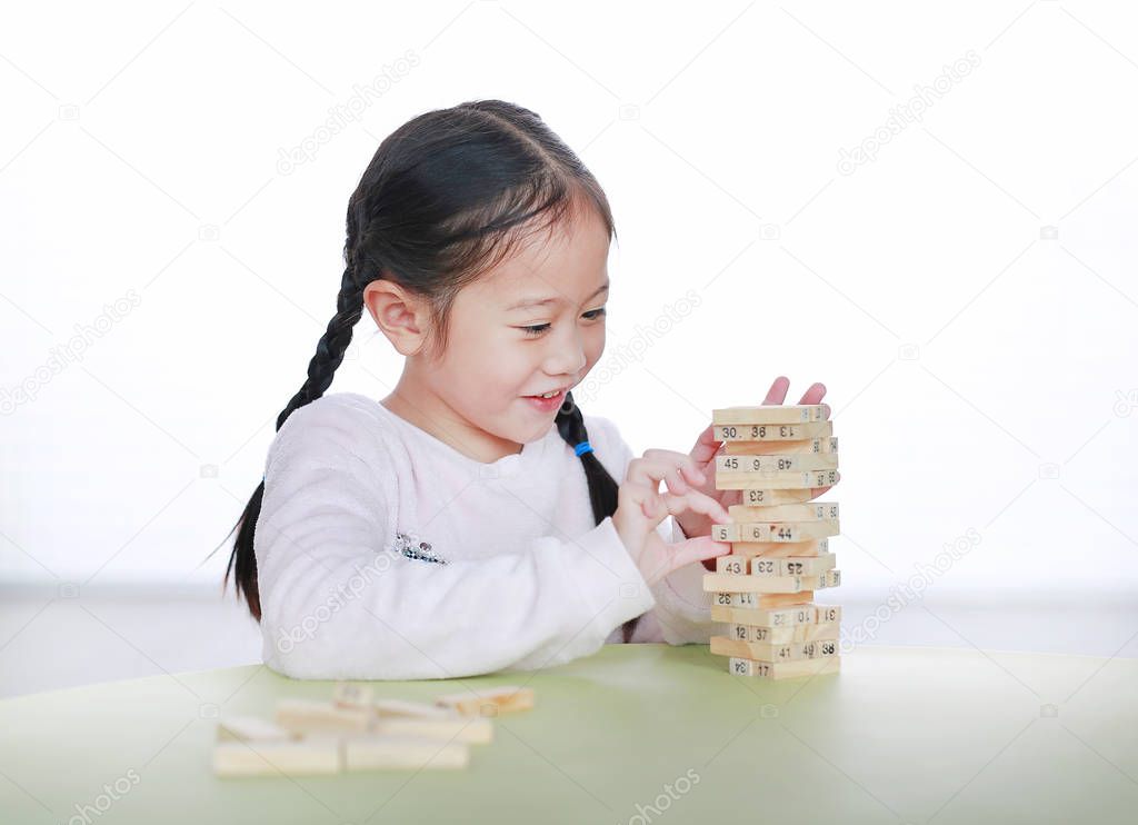 Happy little Asian child girl playing wood blocks tower game for Brain and Physical development skill in a classroom. Focus at children face. Kid imagination and learning concept.