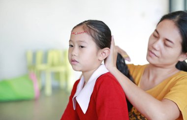 Yakın plan Asyalı anne evde kızının saçını tarıyor..