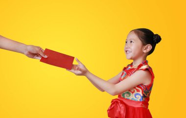 Geleneksel kırmızı cheongsam giyen güzel Asyalı küçük kız sarı arka planda izole edilmiş kırmızı bir zarf aldığı için mutlu. Çin Yeni Yıl Kutlaması.