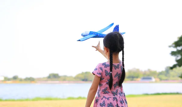 自然の庭で空を飛ぶためにおもちゃの飛行機を投げるアジアの小さな子供の女の子 — ストック写真