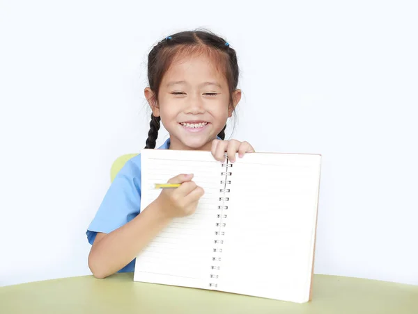 陽気アジアの小さな子供女の子で学校制服ショー書き込み上の空白のノートブック座っ上のデスク隔離された白い背景 — ストック写真