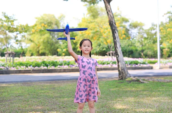快乐的小女孩在户外的花园里 举起一架蓝色的玩具飞机 在空中飞翔 — 图库照片