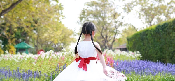 庭の周りの花でリラックス白いドレスの肖像画の女の子 バックビュー — ストック写真