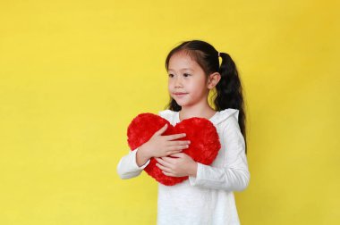 Little girl hugging fluffy red heart on yellow background