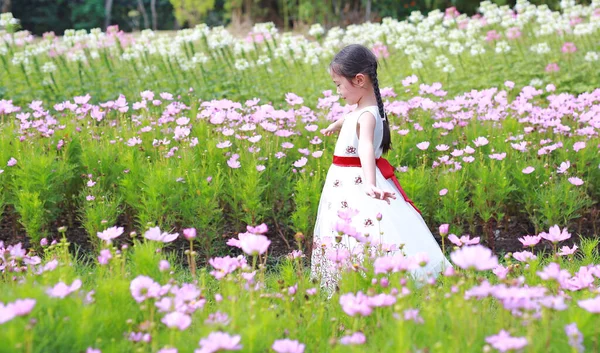 晴れた日に花の庭でリラックスした子供の女の子 公園の屋外で花と一緒に歩く白いドレスのアジアの子供 サイドビュー — ストック写真