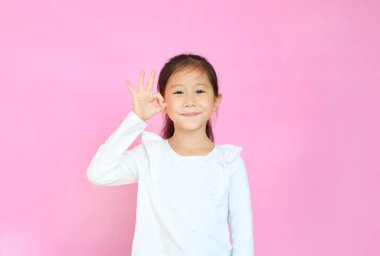 Güzel Asyalı küçük kız pembe arka planda izole edilmiş ok sembolü yapıyor. Kendinden emin el işareti gösteren gülümseyen bir çocuğun portresi. reklam ve insanlar konsepti