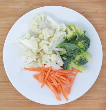 Karnabahar, brokoli ve havuç ahşap arka plan karşı bir plaka üzerinde