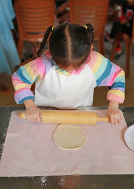 Pizza için Dough 'un üzerinde tahta raptiye kullanan Asyalı küçük kızın portresi. Ev yapımı pizza hazırlama süreci.