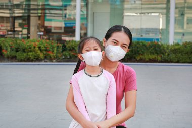 Açık alanda koronavirüsü ve pm2.5 tozunu korumak için maske takan Asyalı anne ve kız portresi. Covid-19 ve hava kirliliği kavramını durdurdu.
