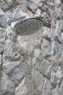 Açık hava yüzme havuzunun yanındaki taş duvarda duş alır..