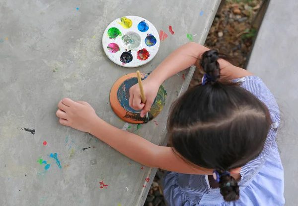 Asian little kid girl painting on earthenware dish. View on top.