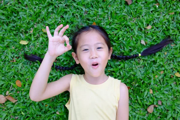 Vacker Asiatisk Liten Flicka Gör Skylt Liggande Grönt Gräs Bakgrund — Stockfoto