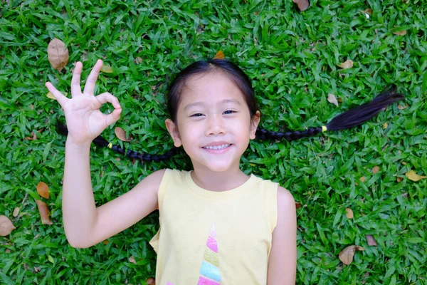 Portret Azjatyckiej Dziewczynki Znak Leżący Zielonym Tle Trawy Uśmiechnięty Dzieciak — Zdjęcie stockowe