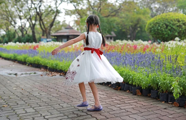 陽気な小さな子供の女の子は踊り 新鮮な花の庭で楽しんでいます 公園の屋外で子供が遊ぶ — ストック写真