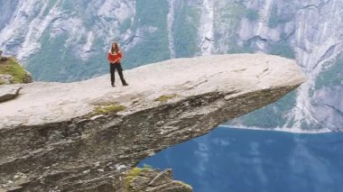 Odda, Norveç. Genç kız bir kayanın üzerinde durarak jimnastik yapıyor. İnsanlar Norveç 'te Bir Rock Trolltunga' nın Üzerinde Dururken Fotoğraf Çekiliyor.