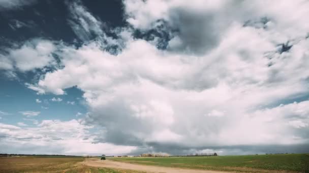 時間の経過雨の前にふわふわの雲と風光明媚な劇的な空の下でフィールド春の牧草地の風景を介して田舎の農村道路のタイムラプス。農業と気象予報の概念 — ストック動画