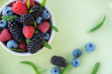 yaban mersini, böğürtlen, ahududu ve nane yaprakları bir ışık yeşil kase