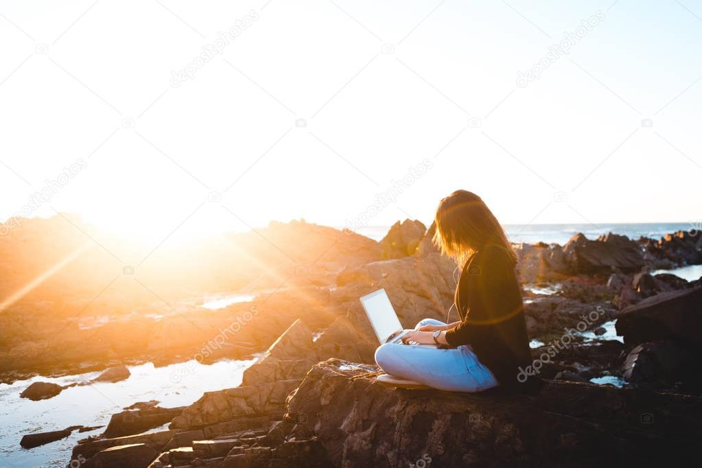 woman using laptop while sitting on seaside