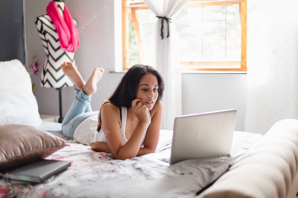 Teenage girl in bedroom looking at laptop