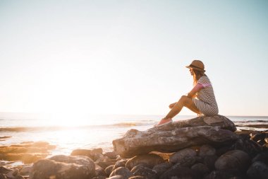 Young woman sitting on beach rocks clipart