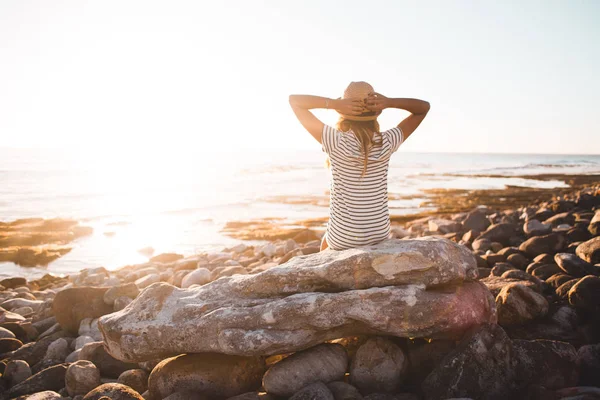 Jonge vrouw zittend op strand rotsen — Stockfoto