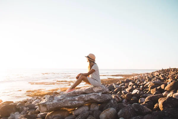 Mujer joven sentada en rocas de playa —  Fotos de Stock