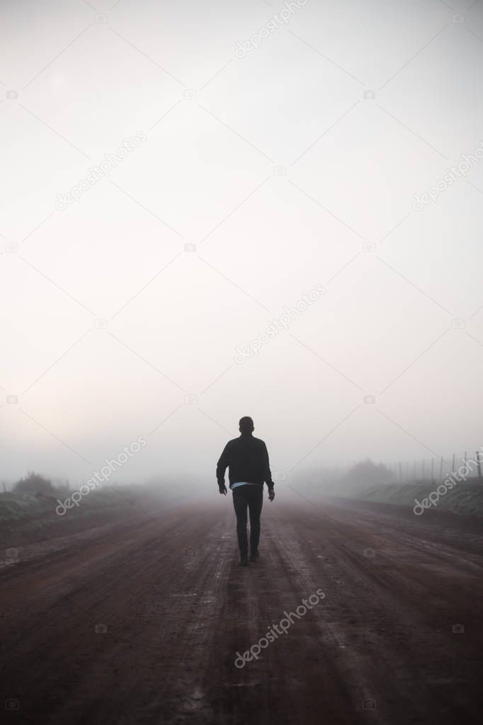 Man walking away on misty road