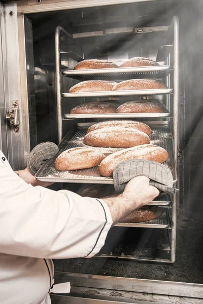 El panadero saca el pan caliente del horno . — Foto de Stock