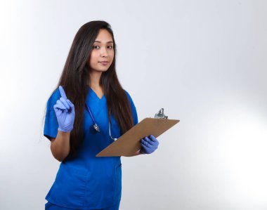 Mavi önlüklü genç bir hemşire bir pano tutuyor ve parmağını kaldırıyor..