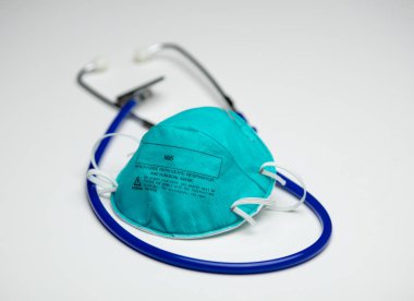 An single teal N95 respirator mask on top of a blue medical stethoscope. Isolated on a white background. clipart