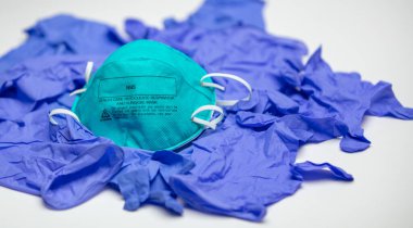 A turquoise N95 particulate respirator and surgical mask on top of many medical gloves. clipart